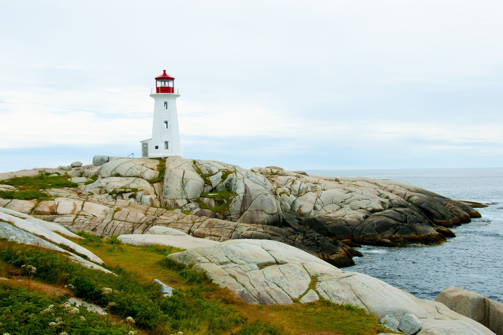 The white and red Peggy's Cove lighthouse on granite rocks by the sea